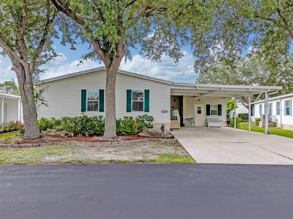 A single-story manufactured home with light siding, green shutters, and a covered carport — 213 NATURES WAY, NORTH PORT, FL