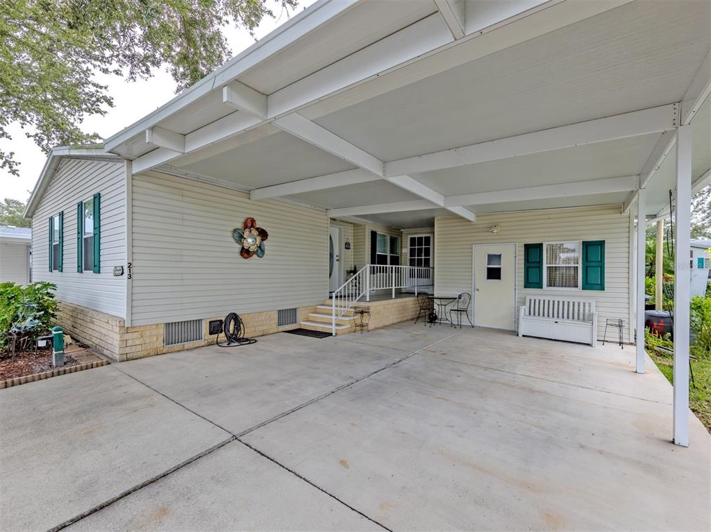 A single-story house with light siding, green shutters, and a large covered concrete carport — 213 NATURES WAY, NORTH PORT, FL