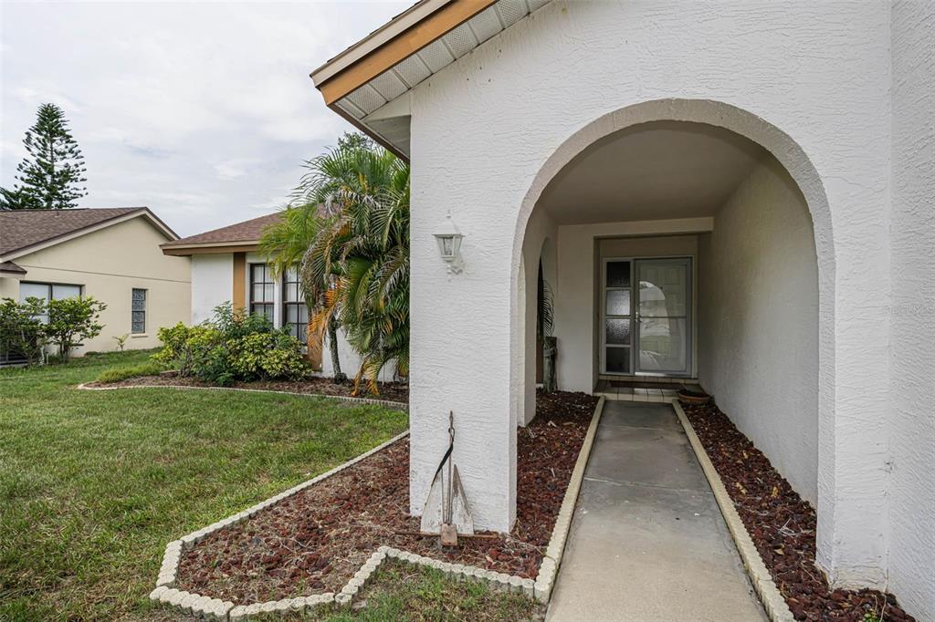 A white stucco house features an arched entryway and a concrete walkway leading to the door — 3114 SUMMERVALE DRIVE, HOLIDAY, FL