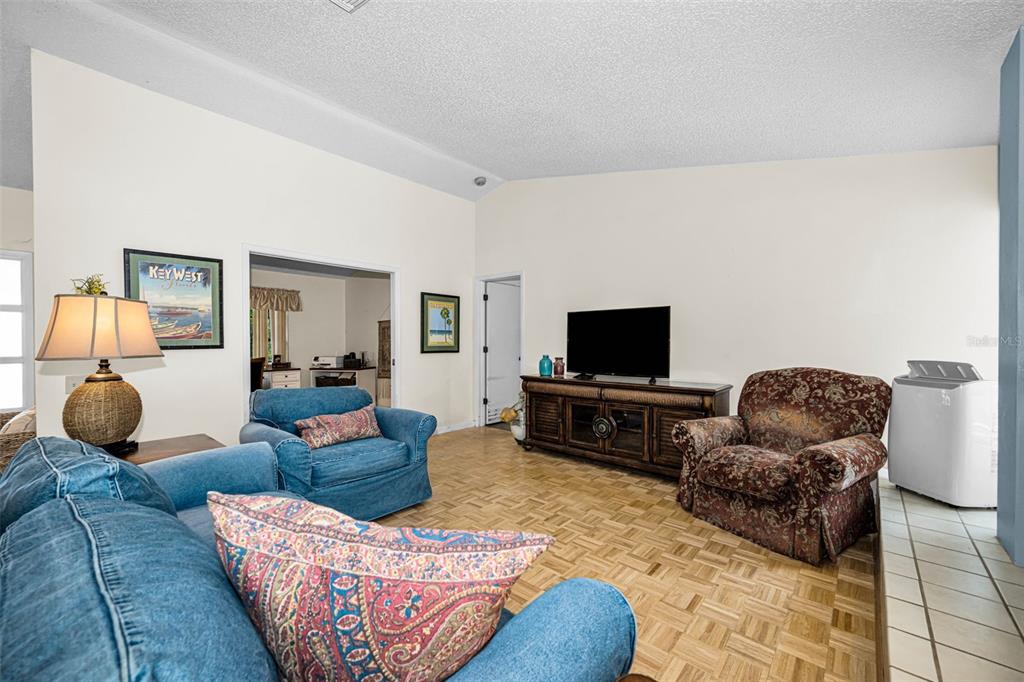 A living room with a vaulted ceiling, parquet flooring, blue and patterned armchairs, and television — 3114 SUMMERVALE DRIVE, HOLIDAY, FL