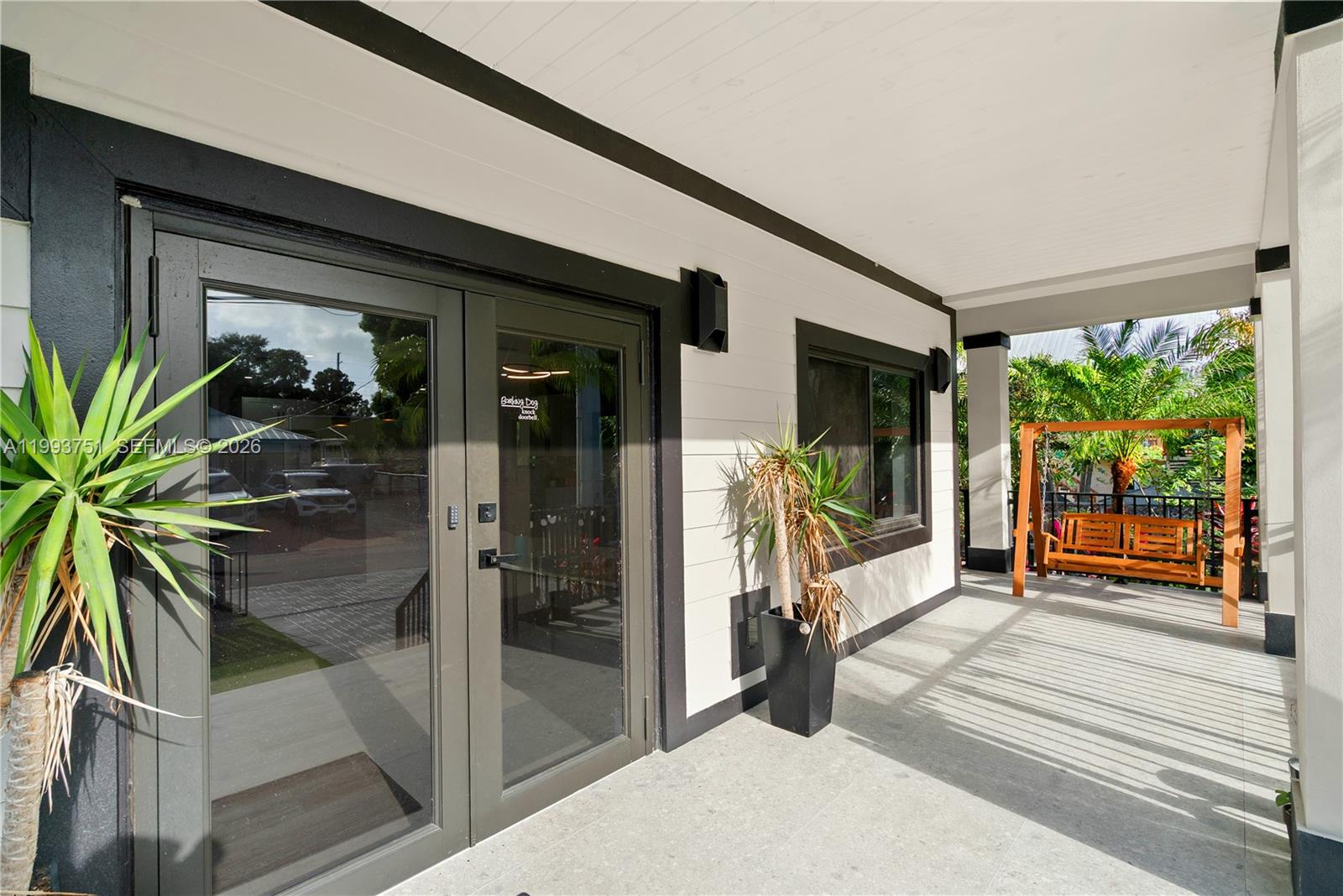 A covered porch features a glass double door, a potted plant, and a wooden swing — 13 Coral Way, Key Largo FL 33037, KEY LARGO, FL