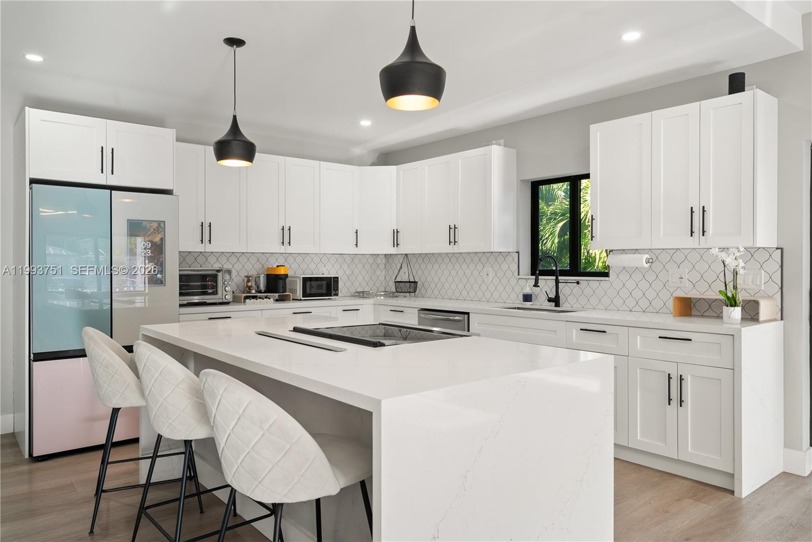A modern kitchen features white cabinetry, a large waterfall island, and two black pendant lights — 13 Coral Way, Key Largo FL 33037, KEY LARGO, FL