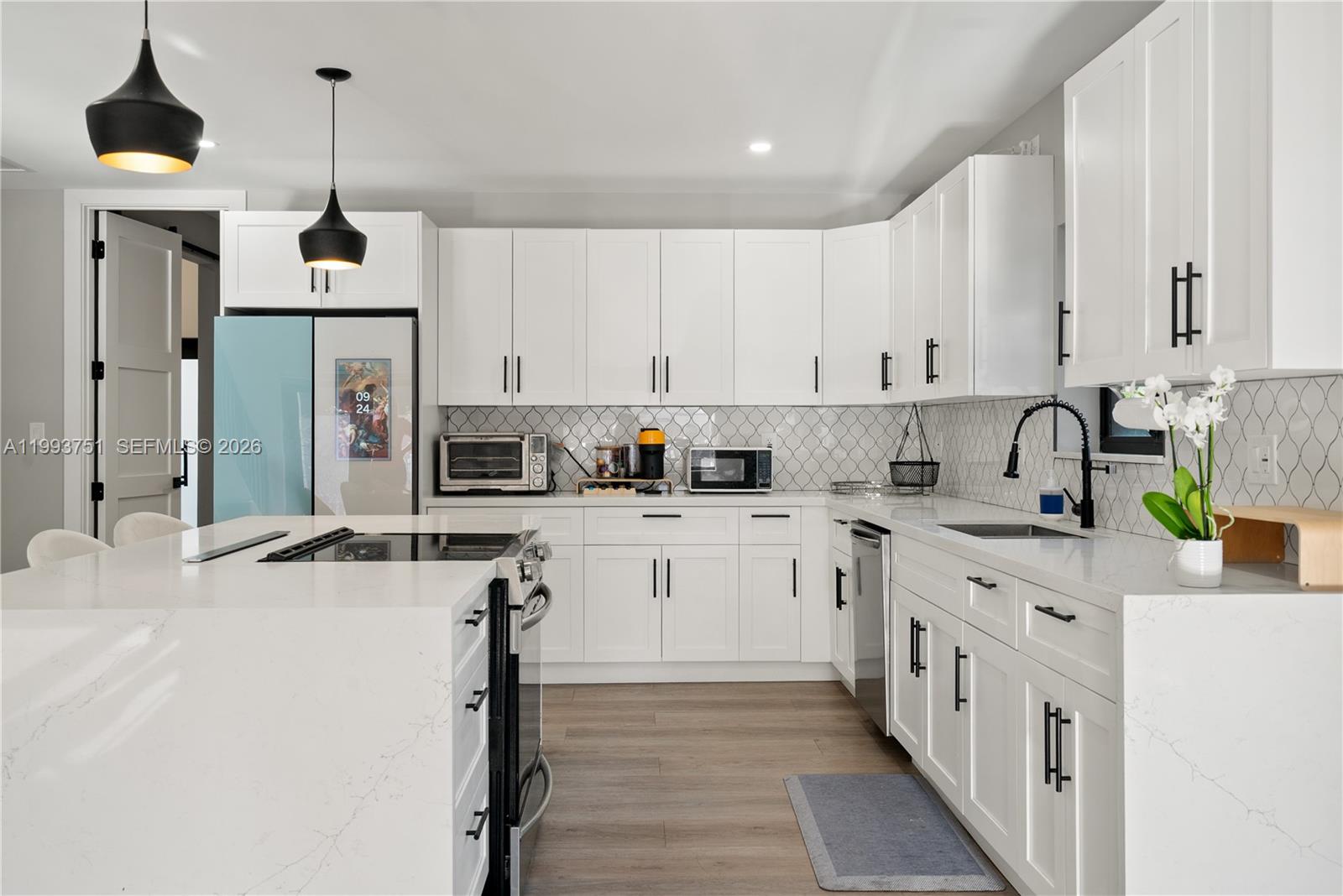 A modern kitchen features white cabinetry, quartz countertops, a central island, and black hardware — 13 Coral Way, Key Largo FL 33037, KEY LARGO, FL