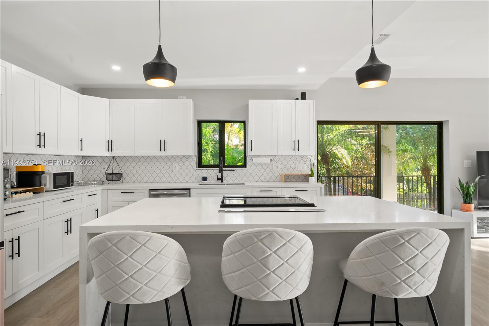 A modern kitchen features white cabinetry, a large quartz island with seating, and pendant lighting — 13 Coral Way, Key Largo FL 33037, KEY LARGO, FL