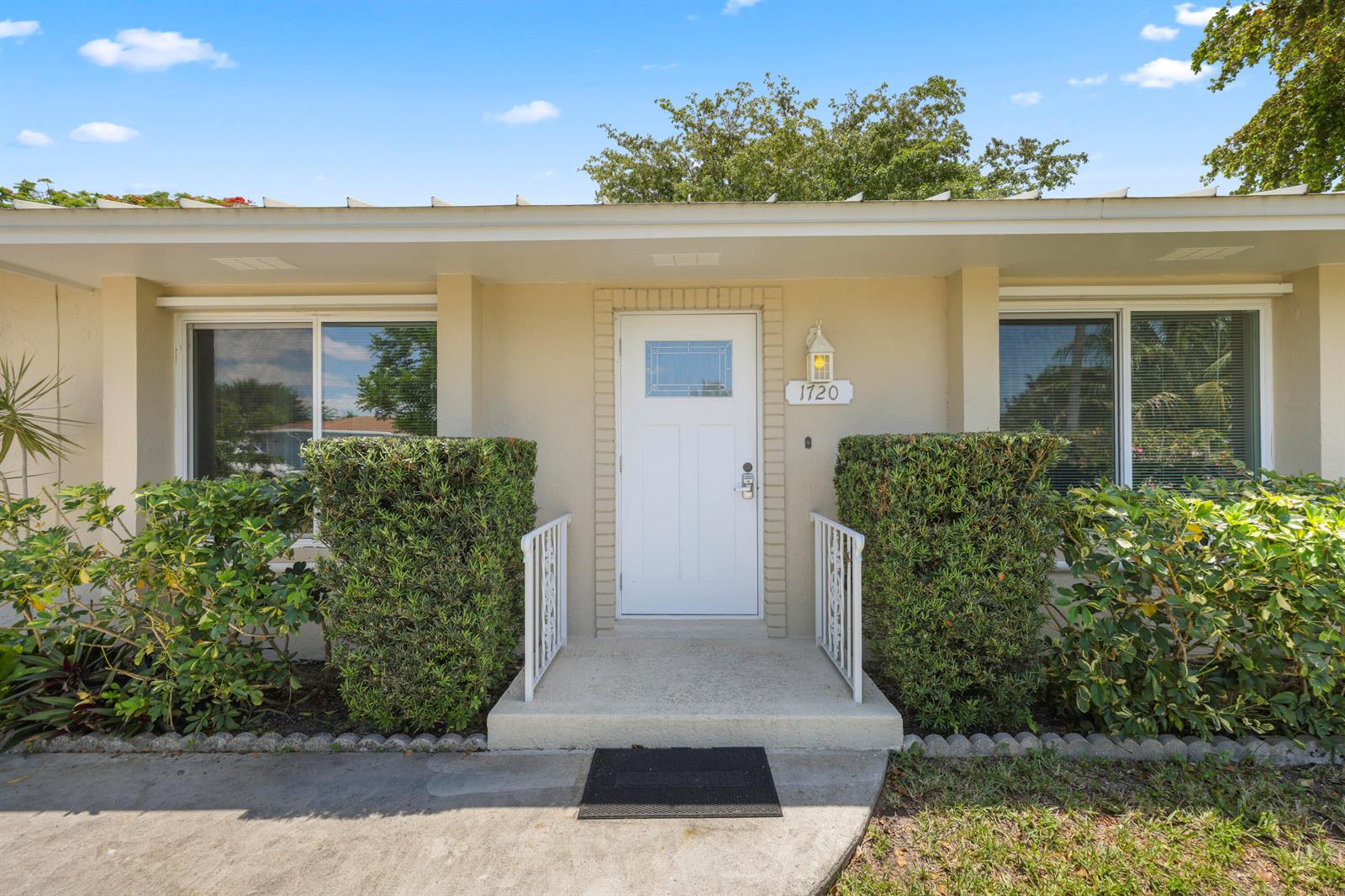 The exterior of a single-story house features a white front door, windows, and manicured hedges — 1720 SW 10th Street, Boca Raton FL 33486, BOCA RATON, FL
