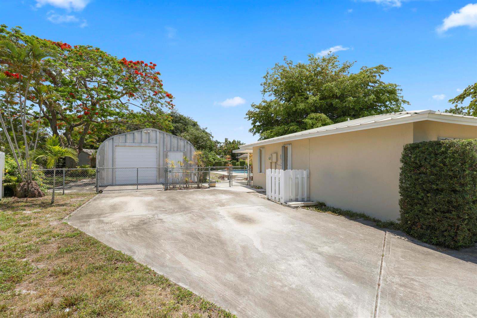 A concrete driveway leads to a metal garage and the side of a beige house — 1720 SW 10th Street, Boca Raton FL 33486, BOCA RATON, FL