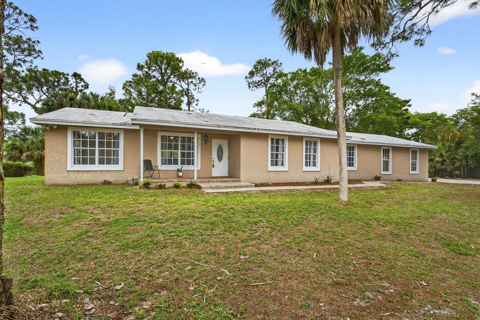 A single-story tan stucco house with a white front door and multiple windows — 16932 Okeechobee Boulevard, FL 33470, FL