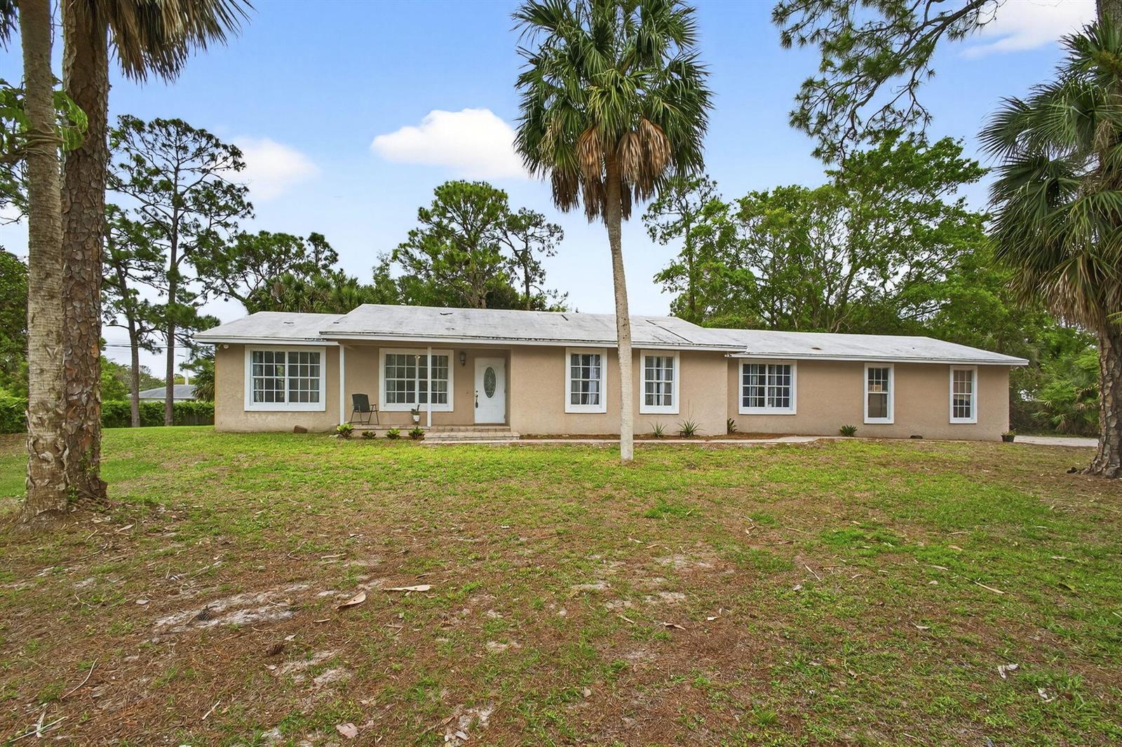 A single-story, beige stucco house with a white front door and multiple windows — 16932 Okeechobee Boulevard, FL 33470, FL