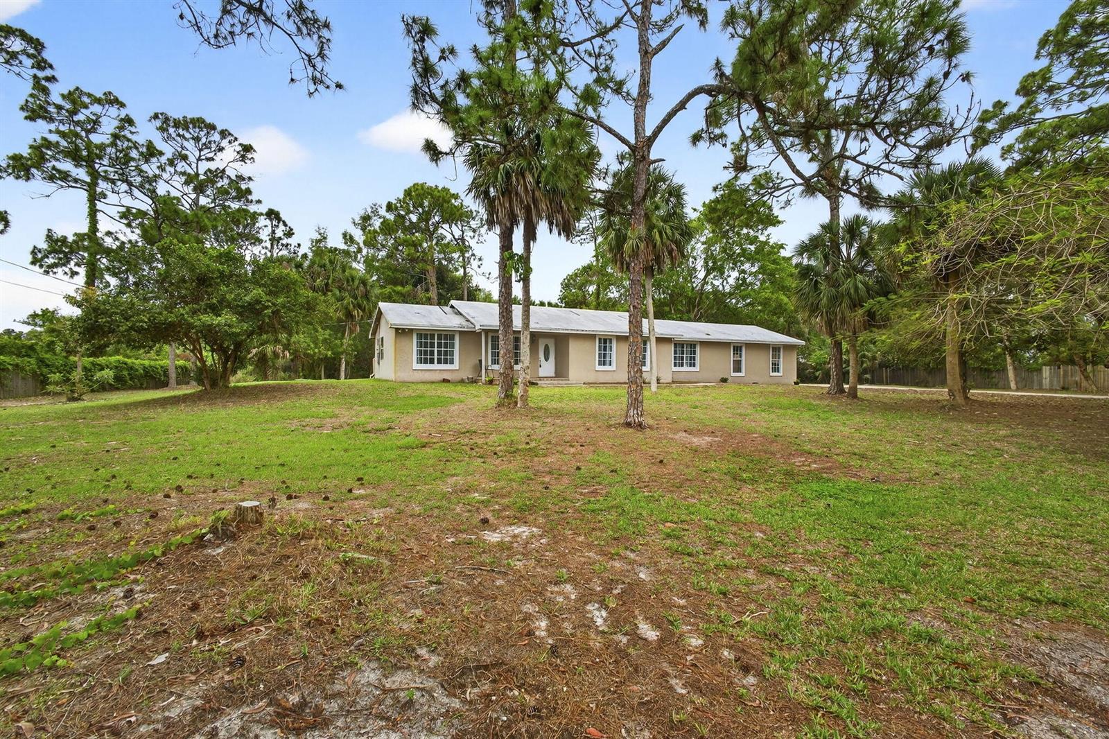 A single-story house with a light-colored exterior sits on a large, grassy, tree-filled lot — 16932 Okeechobee Boulevard, FL 33470, FL