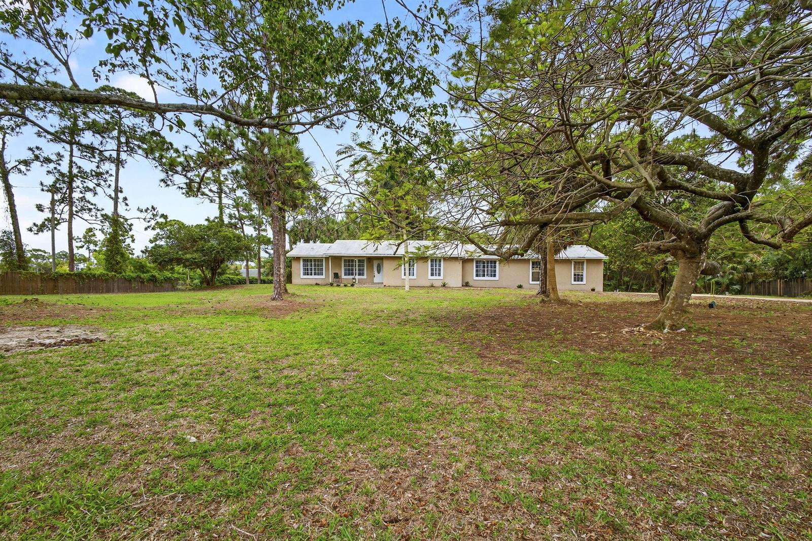 A single-story house with a light-colored exterior sits on a large, grassy, tree-filled lot — 16932 Okeechobee Boulevard, FL 33470, FL