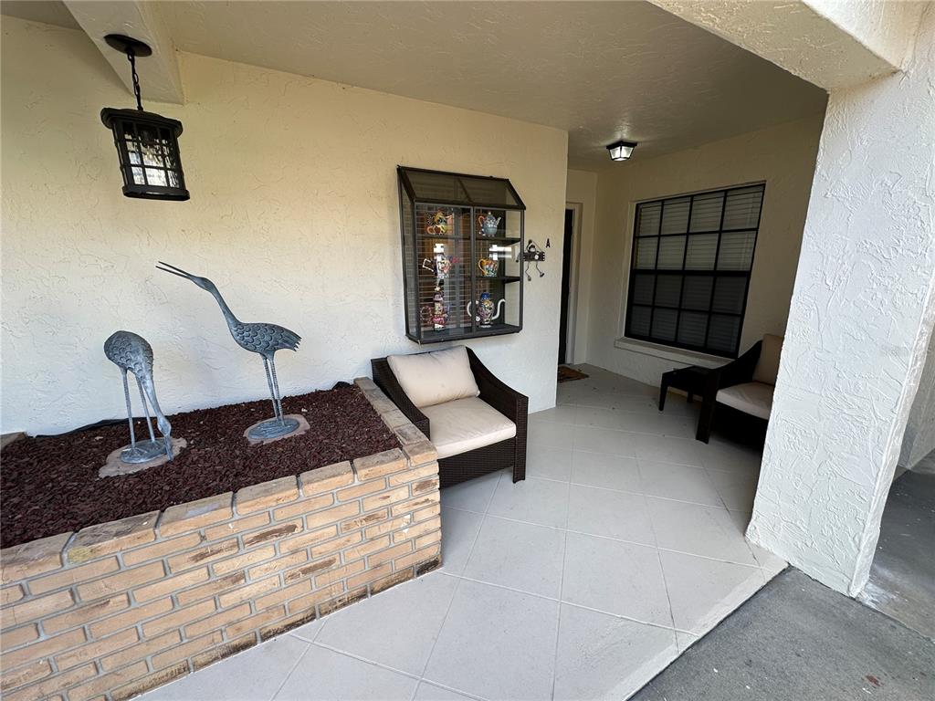 A covered patio features a brick planter with bird statues, wicker seating, and wall-mounted shelving — 760 AVENIDA ESTANCIA UNIT 217, VENICE, FL
