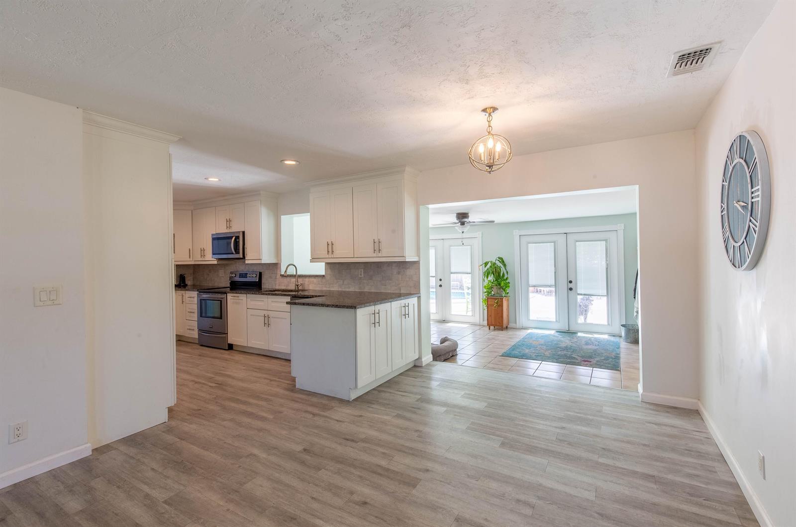 A kitchen with white cabinets and dark countertops opens into a sunroom with tiled floors — 12069 Easterly Avenue, Palm Beach Gardens FL 33410, PALM BEACH GARDENS, FL