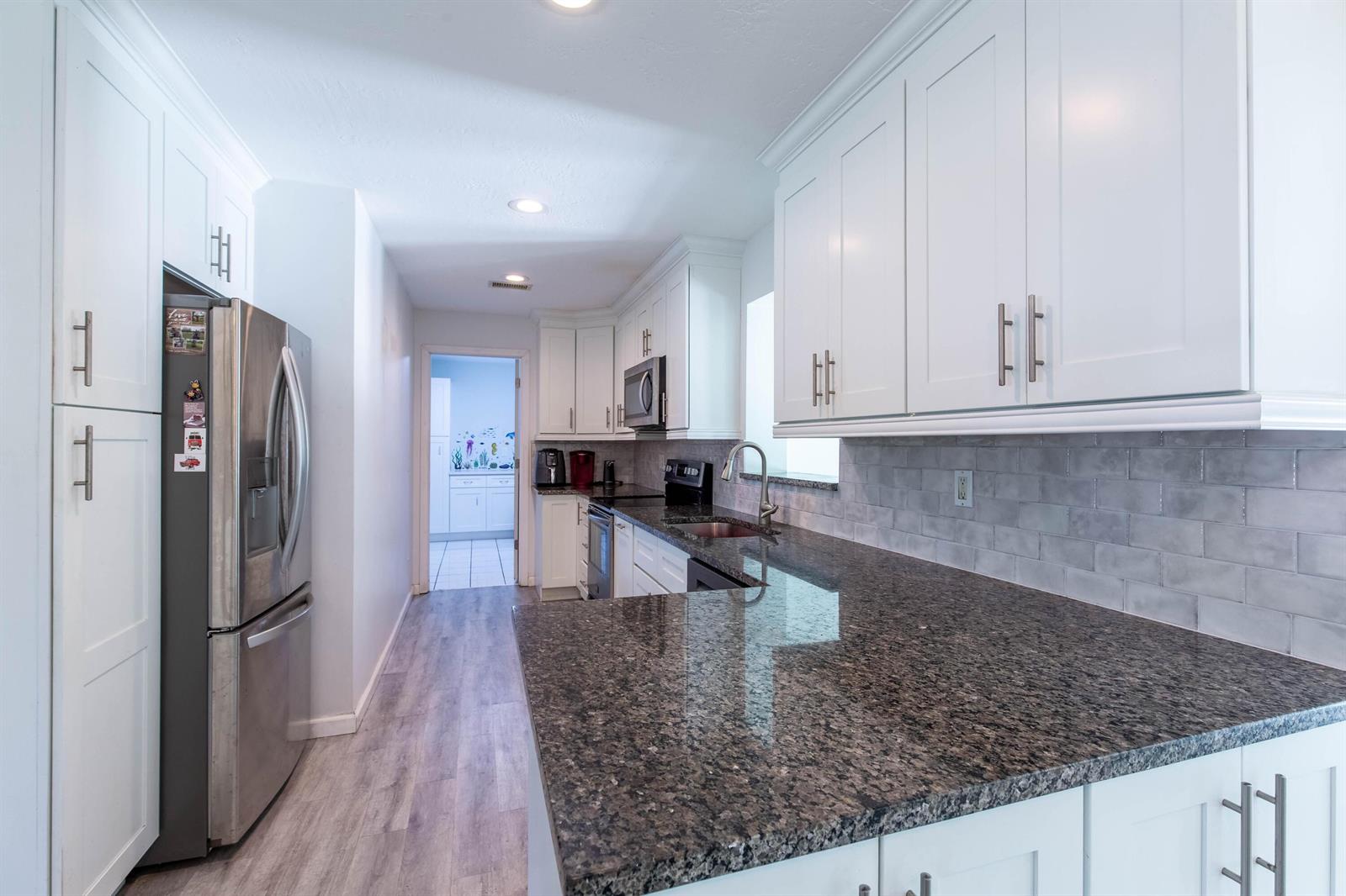 A kitchen with white cabinets, dark granite countertops, stainless steel appliances, and gray subway tile — 12069 Easterly Avenue, Palm Beach Gardens FL 33410, PALM BEACH GARDENS, FL