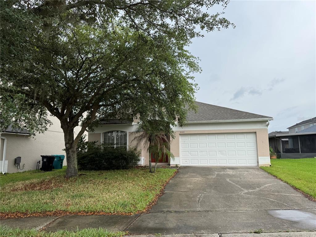 A single-story house with a white garage door, a concrete driveway, and a large tree — 5004 ADAIR OAK DRIVE, ORLANDO, FL