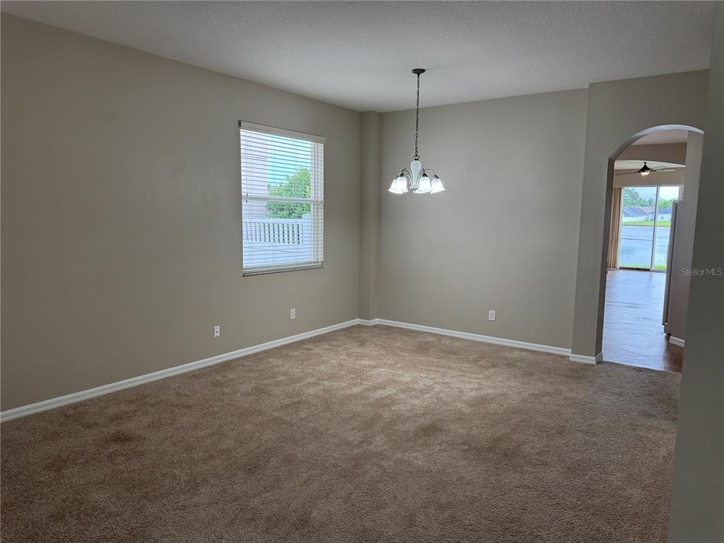 An empty dining room features beige carpet, neutral walls, a window, and a hanging chandelier — 5004 ADAIR OAK DRIVE, ORLANDO, FL