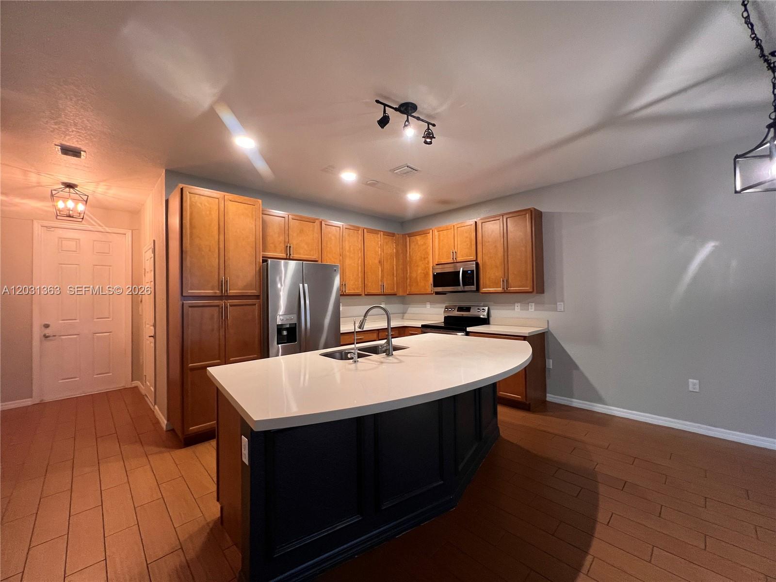 A kitchen features wood cabinets, a dark island with a white countertop, and tile flooring — 4764 E Station Sq, Davie FL 33314, DAVIE, FL