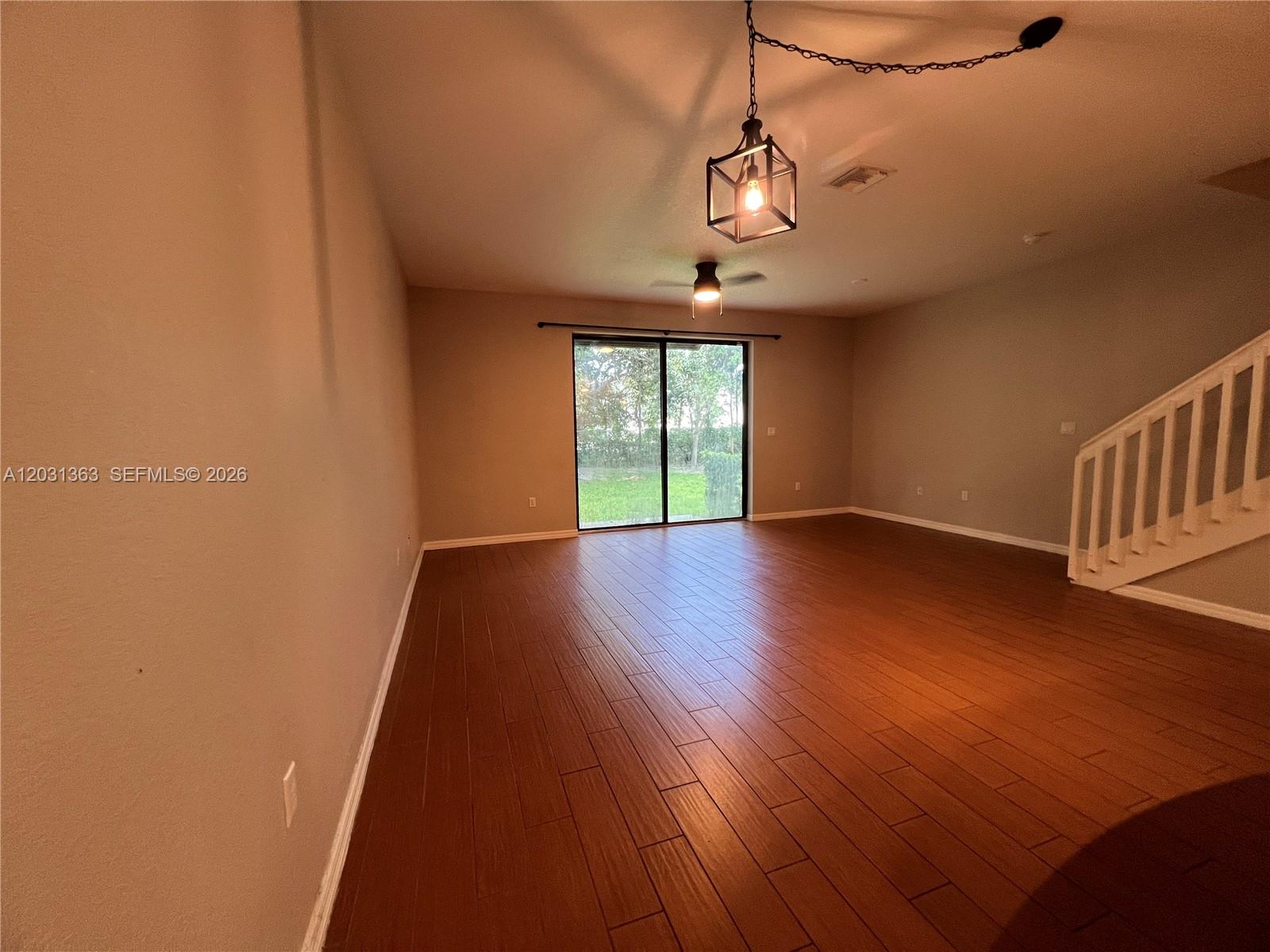 A spacious living room features wood-look tile flooring, a ceiling fan, and sliding glass doors — 4764 E Station Sq, Davie FL 33314, DAVIE, FL