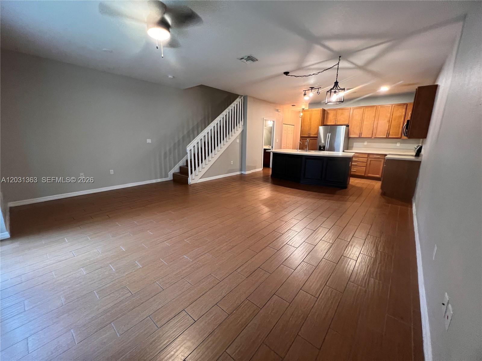 An open-concept living area features wood-look tile flooring, a staircase, and a kitchen island — 4764 E Station Sq, Davie FL 33314, DAVIE, FL
