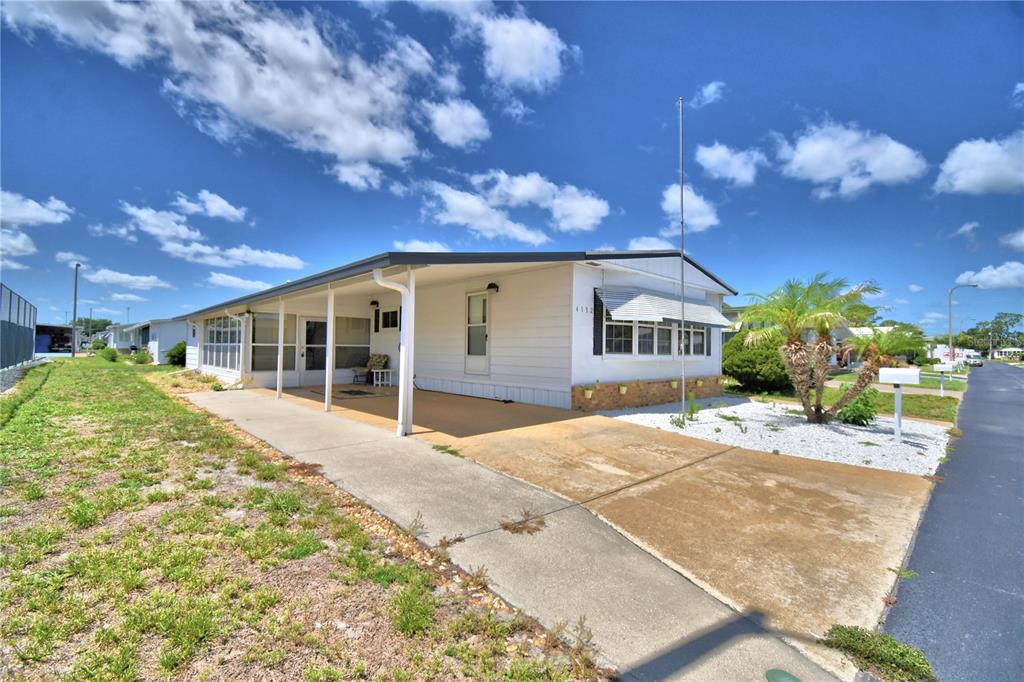 A white mobile home with a carport and a concrete driveway under a blue sky — 4132 SPRUCEWOOD STREET, WINTER HAVEN, FL