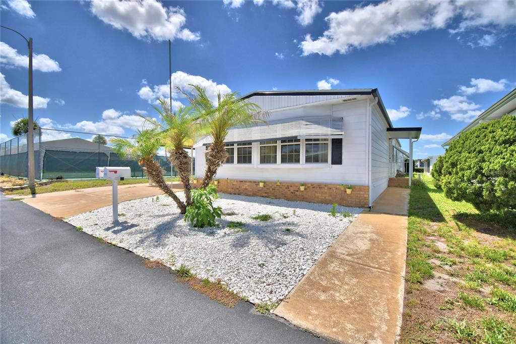 A white manufactured home features a brick base, white rock landscaping, and palm trees — 4132 SPRUCEWOOD STREET, WINTER HAVEN, FL