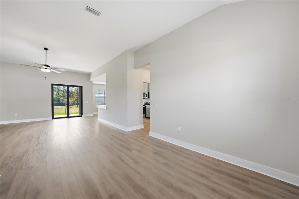 An empty living area with light wood-look flooring, a ceiling fan, and a sliding glass door — 5104 MUNHALL STREET, PORT CHARLOTTE, FL