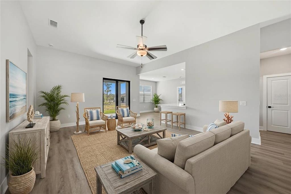 A bright living room features light gray walls, wood-look flooring, a ceiling fan, and furniture — 5104 MUNHALL STREET, PORT CHARLOTTE, FL