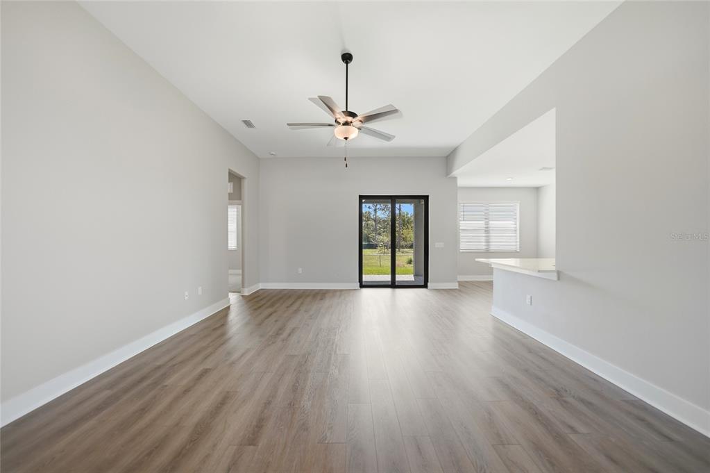 An empty living room features light gray walls, wood-look flooring, a ceiling fan, and sliding doors — 5104 MUNHALL STREET, PORT CHARLOTTE, FL
