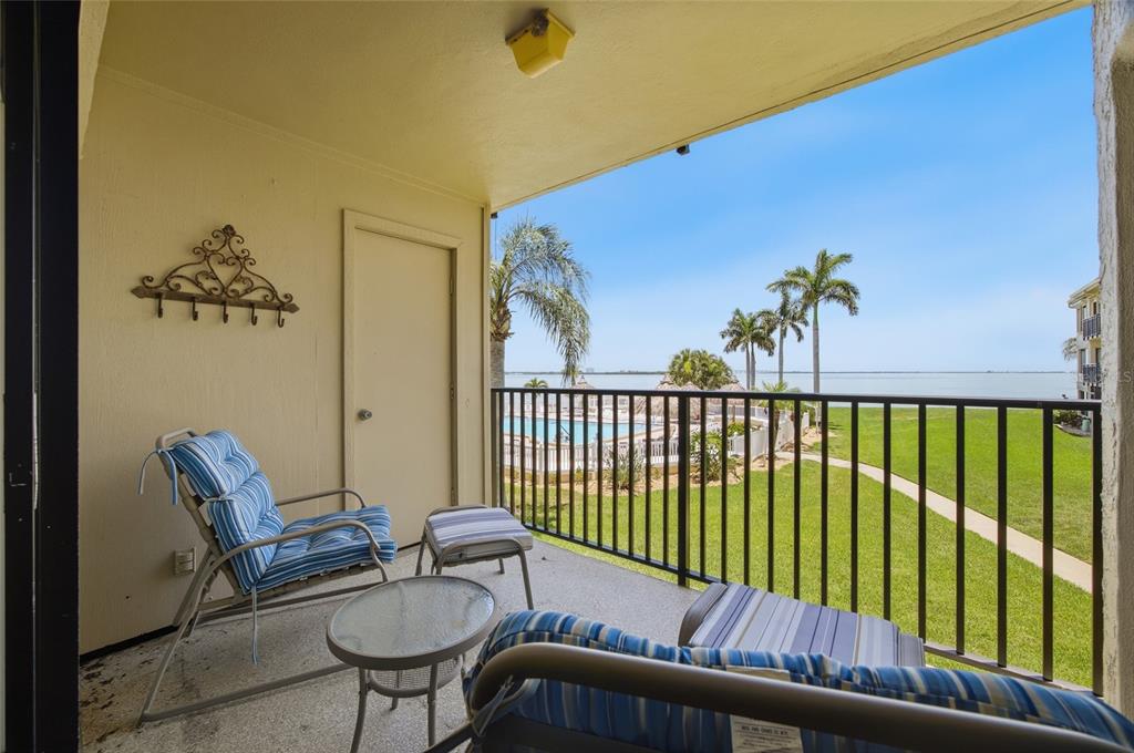 A covered balcony features patio furniture, a metal railing, and a view of a pool and water — 6322 PALMA DEL MAR BOULEVARD S UNIT 216, ST PETERSBURG, FL