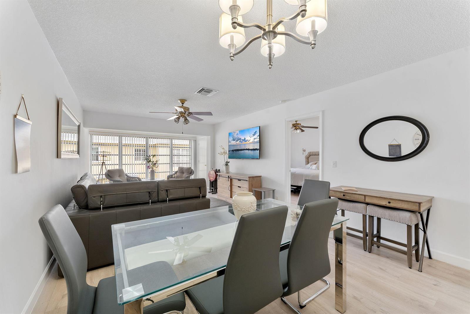 A dining area with a glass table and gray chairs opens into a living room — 1110 Boxwood Drive # 202, Delray Beach FL 33445, DELRAY BEACH, FL