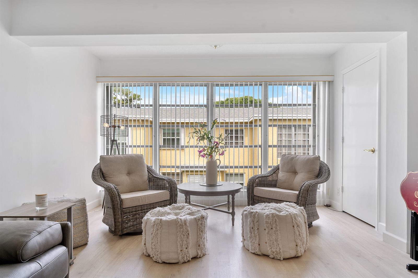 A bright living area features two wicker armchairs, a round table, and two textured poufs — 1110 Boxwood Drive # 202, Delray Beach FL 33445, DELRAY BEACH, FL