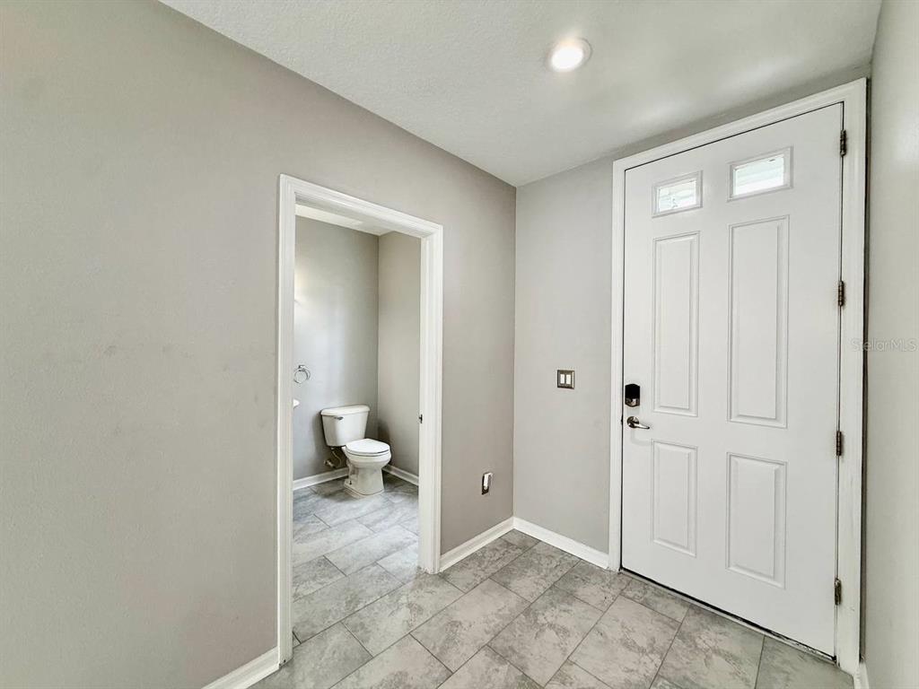 An entryway with gray tile flooring, a white front door, and a view into a bathroom — 10653 MARSHA DRIVE, NEW PORT RICHEY, FL