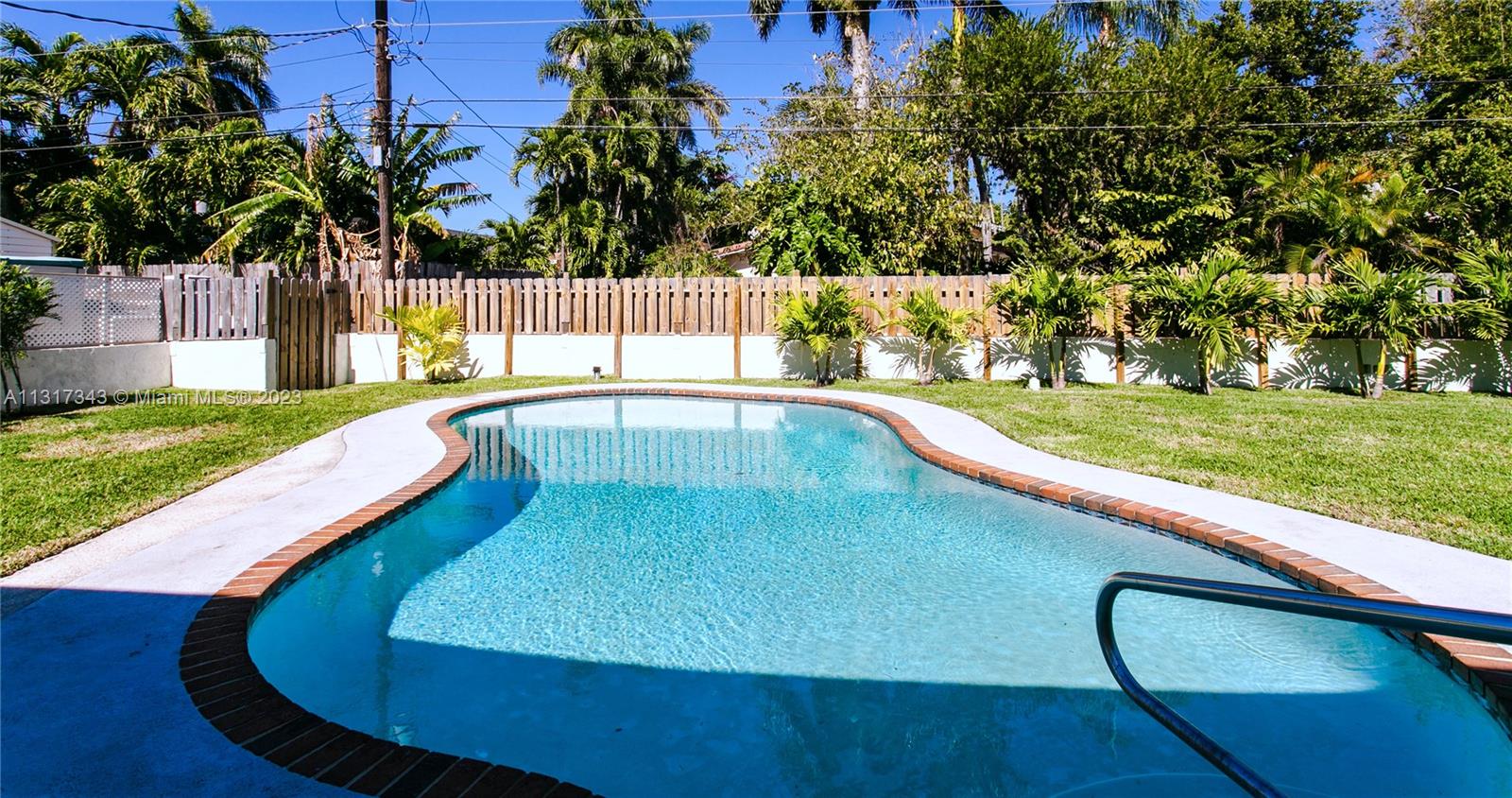 A backyard features a kidney-shaped swimming pool surrounded by a lawn and a wooden fence — 951 Washington St, Hollywood FL 33019, HOLLYWOOD, FL