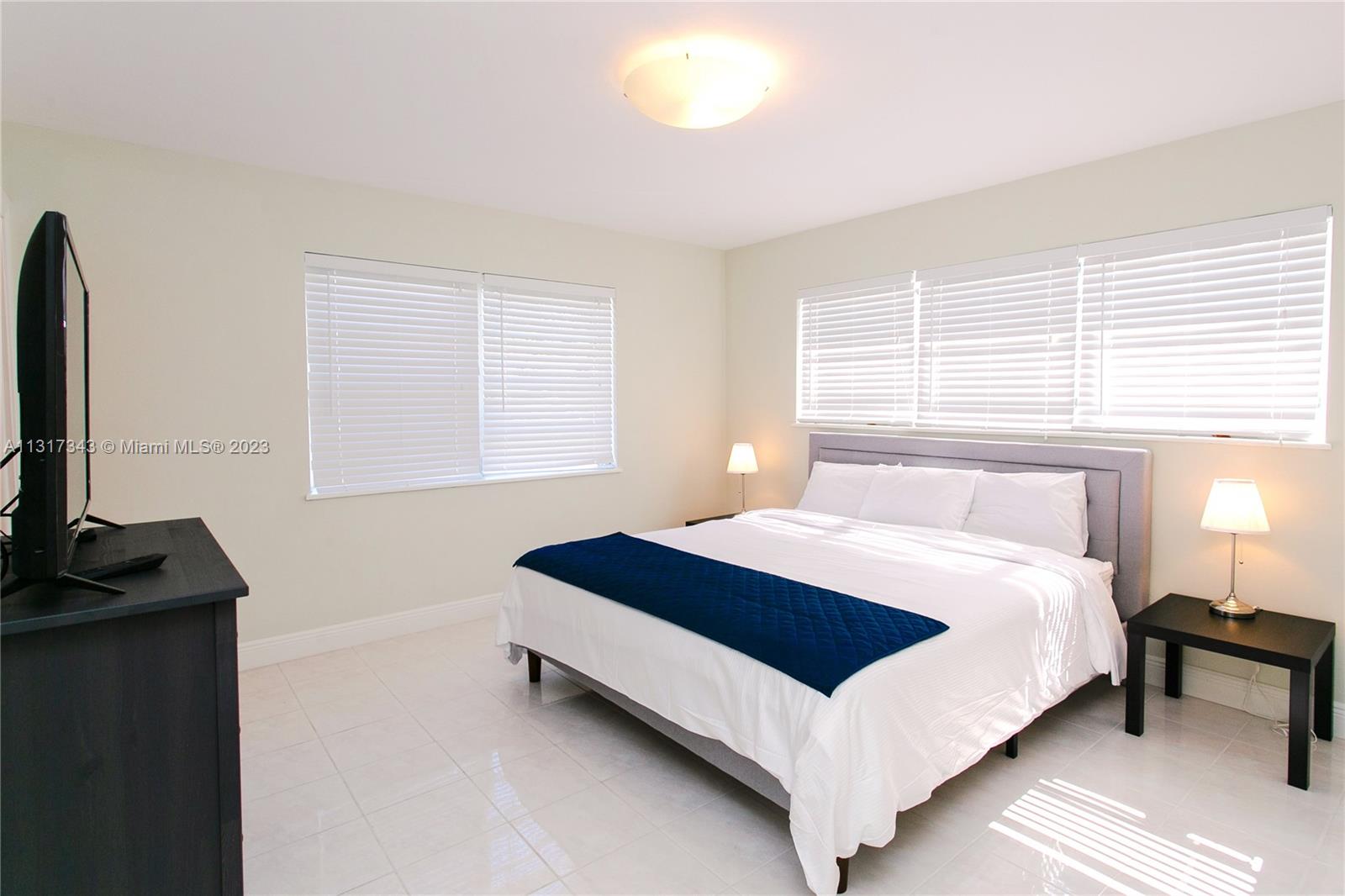 A bedroom features a bed with a blue runner, two side tables, and a television — 951 Washington St, Hollywood FL 33019, HOLLYWOOD, FL