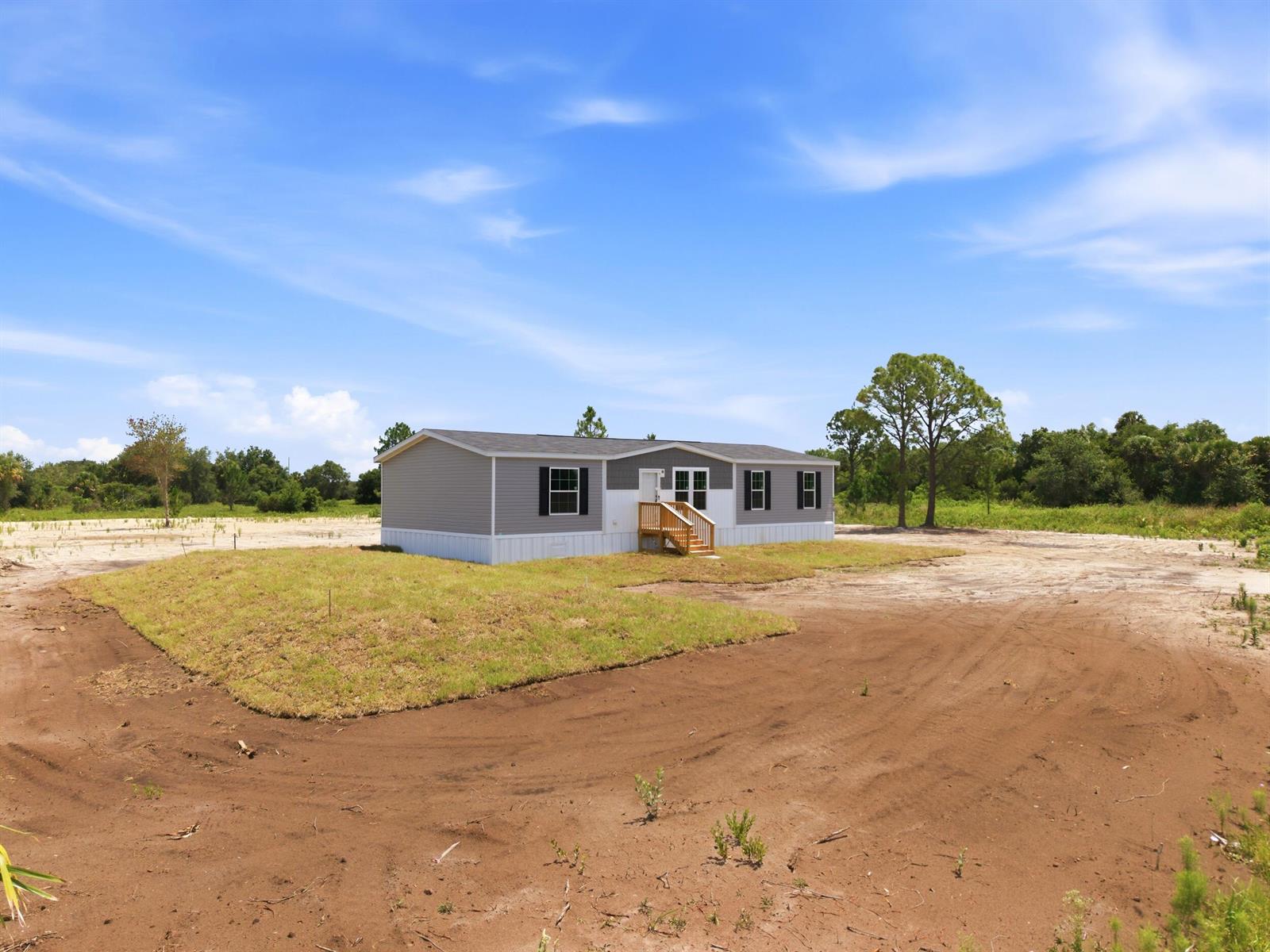 A gray manufactured home sits on a dirt lot with a small patch of grass — 17975 NW 266th Street, Okeechobee FL 34972, OKEECHOBEE, FL