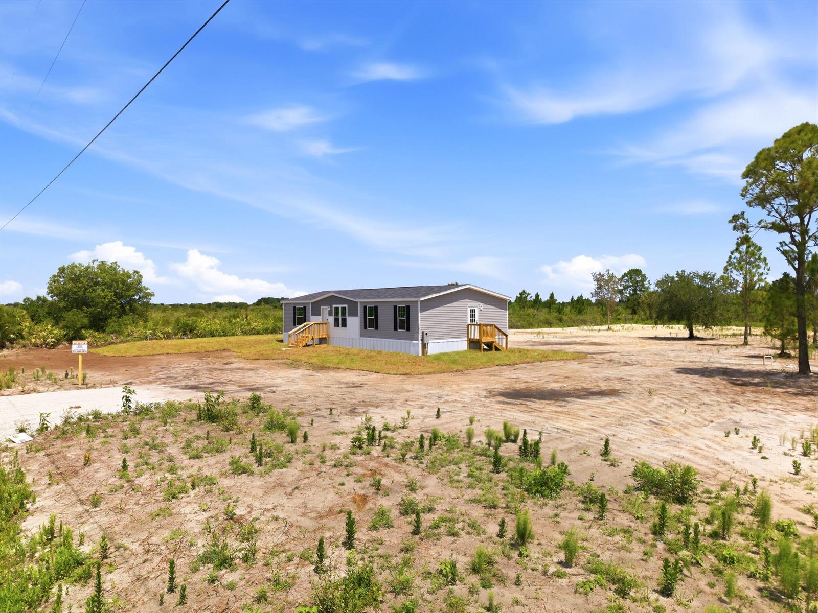 A single-story manufactured home sits on a large, sandy lot under a blue sky — 17975 NW 266th Street, Okeechobee FL 34972, OKEECHOBEE, FL