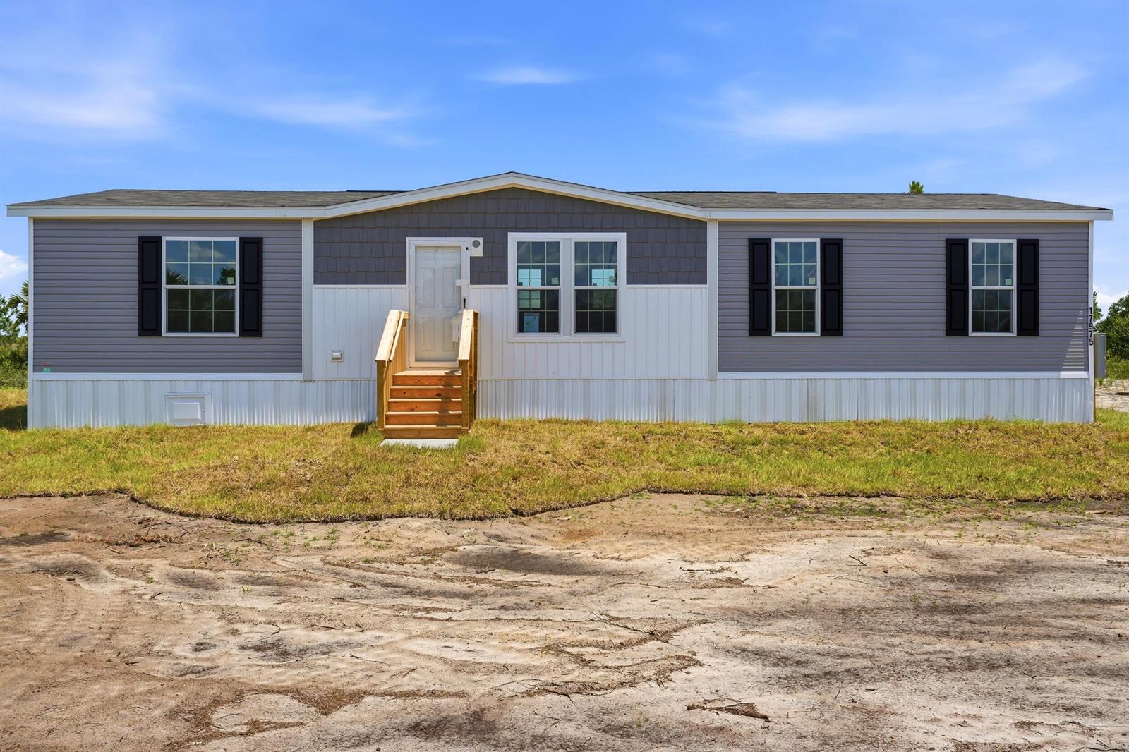 A single-story manufactured home with grey and white siding sits on a dirt lot — 17975 NW 266th Street, Okeechobee FL 34972, OKEECHOBEE, FL