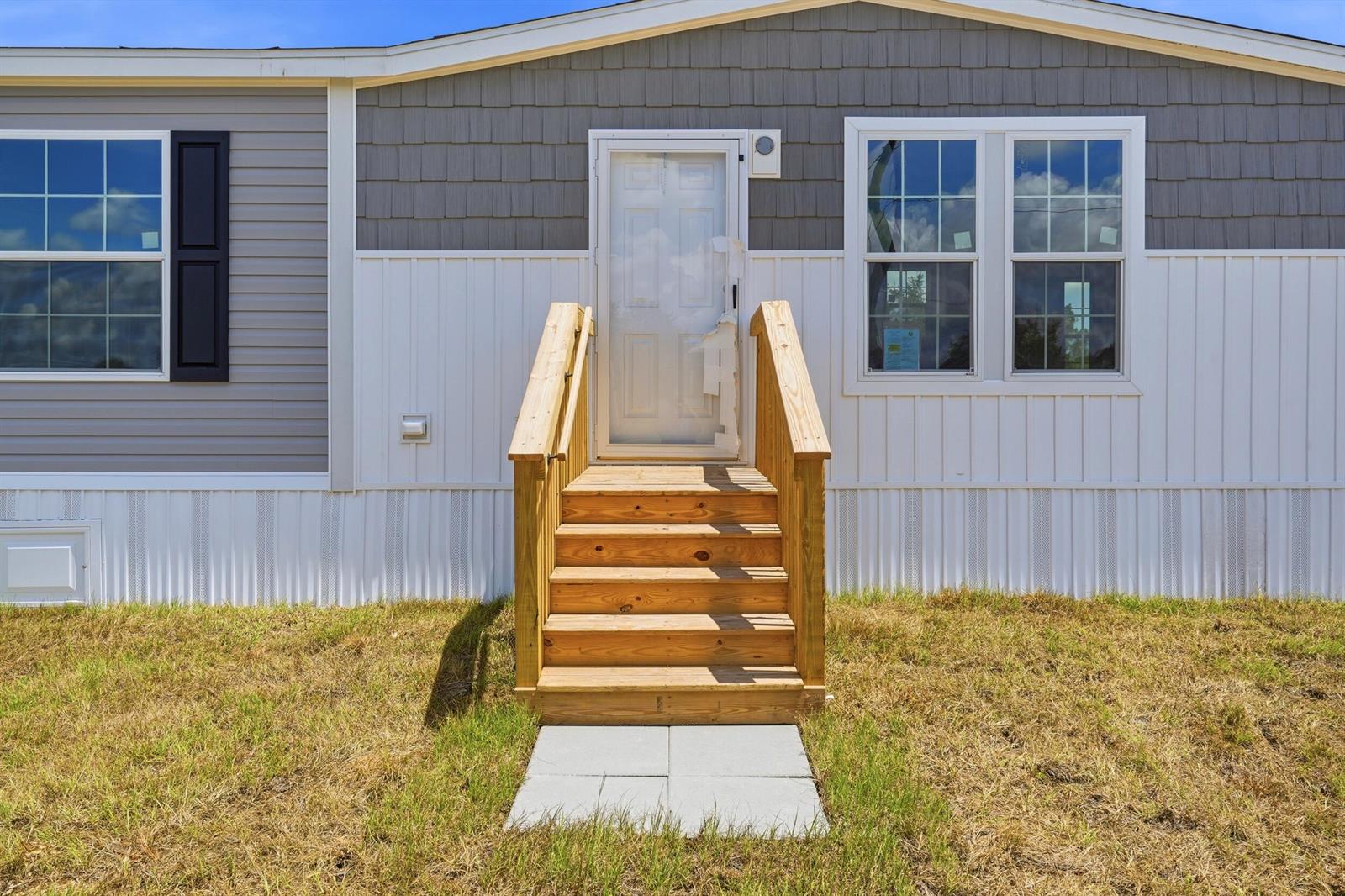 A wooden staircase leads to the front door of a house with gray and white siding — 17975 NW 266th Street, Okeechobee FL 34972, OKEECHOBEE, FL