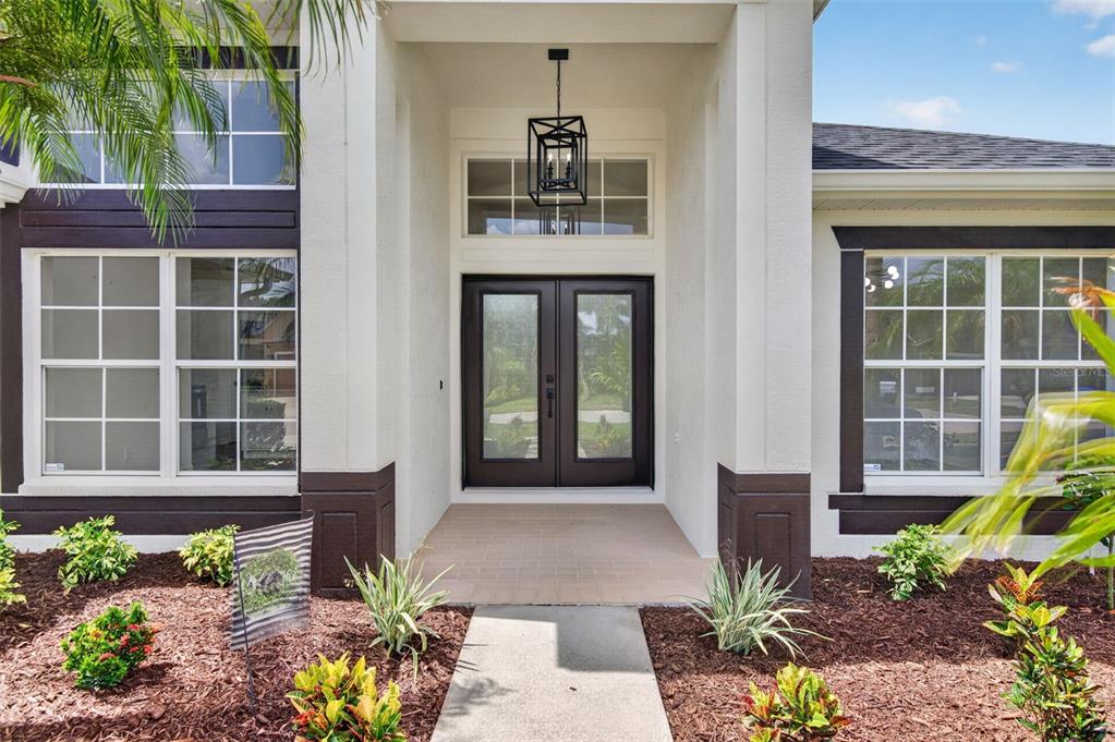 The exterior entrance of a house features a double door, a lantern, and landscaping — 7705 NOTTINGHILL SKY DRIVE, APOLLO BEACH, FL