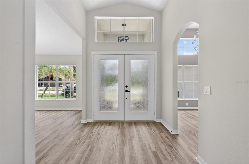 An entryway with light wood-look flooring, double glass-paneled doors, and a high vaulted ceiling — 7705 NOTTINGHILL SKY DRIVE, APOLLO BEACH, FL