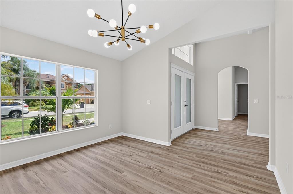 A bright dining room features wood-look flooring, a modern chandelier, and a large front window — 7705 NOTTINGHILL SKY DRIVE, APOLLO BEACH, FL