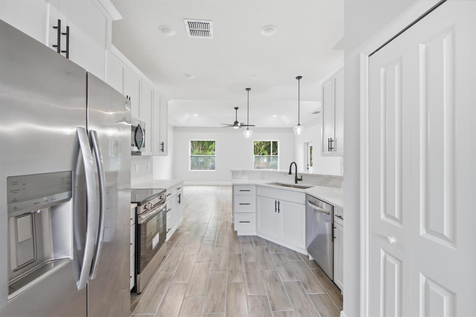 A modern kitchen features white cabinetry, stainless steel appliances, and light wood-look tile flooring — 8780 92nd Avenue, Vero Beach FL 32967, VERO BEACH, FL