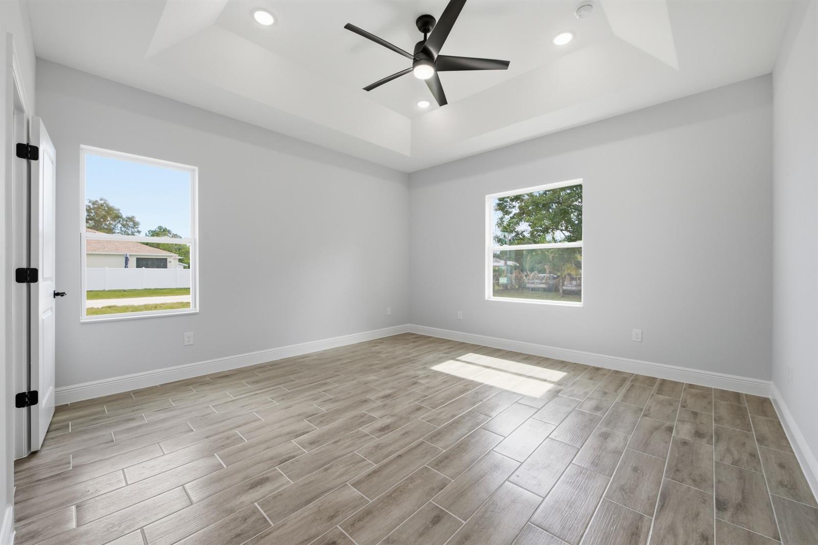 An empty bedroom features light gray walls, wood-look tile flooring, and a tray ceiling — 8780 92nd Avenue, Vero Beach FL 32967, VERO BEACH, FL