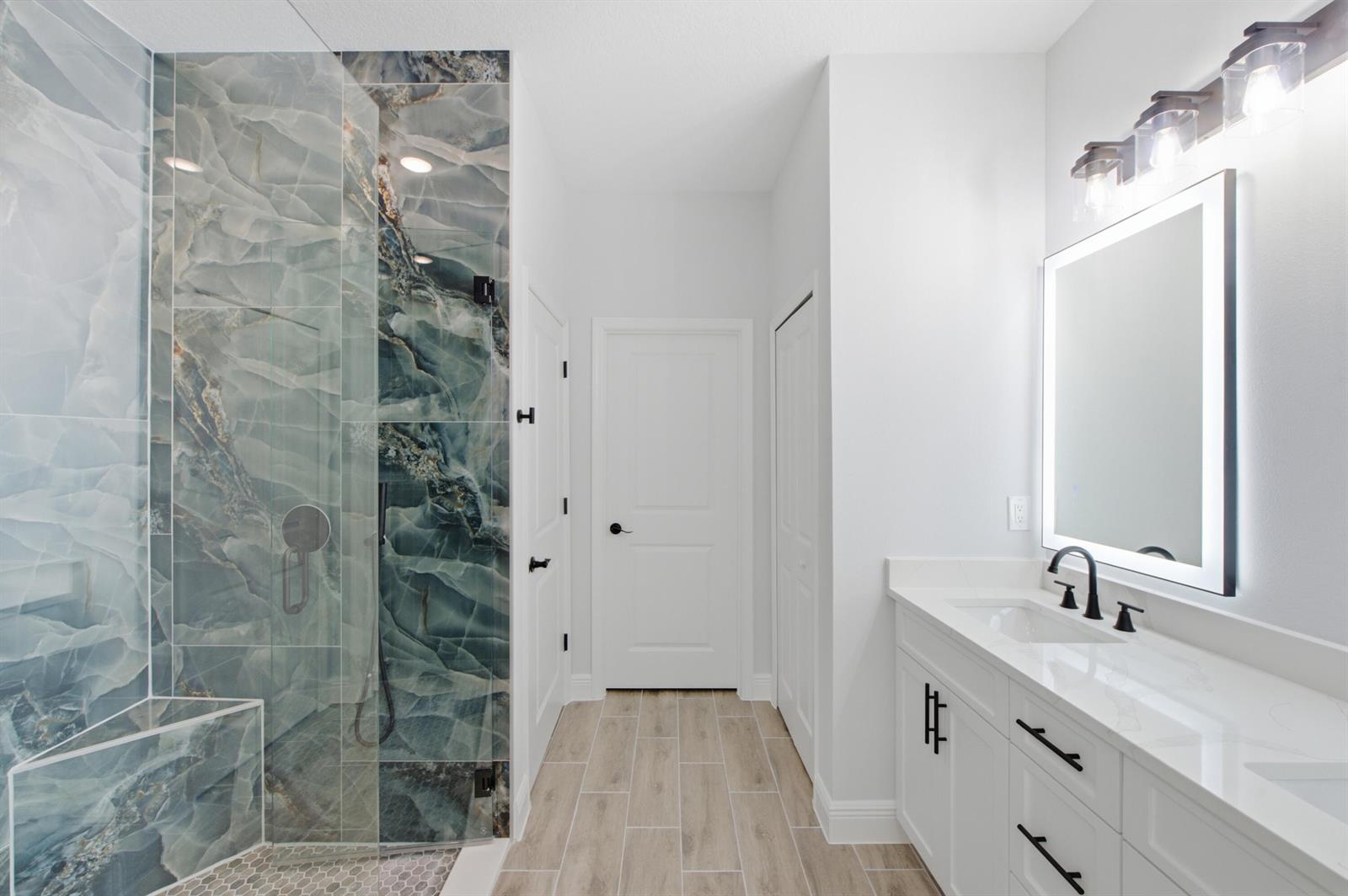A modern bathroom features a blue marble-tiled shower, white vanity, and light wood-look flooring — 8780 92nd Avenue, Vero Beach FL 32967, VERO BEACH, FL