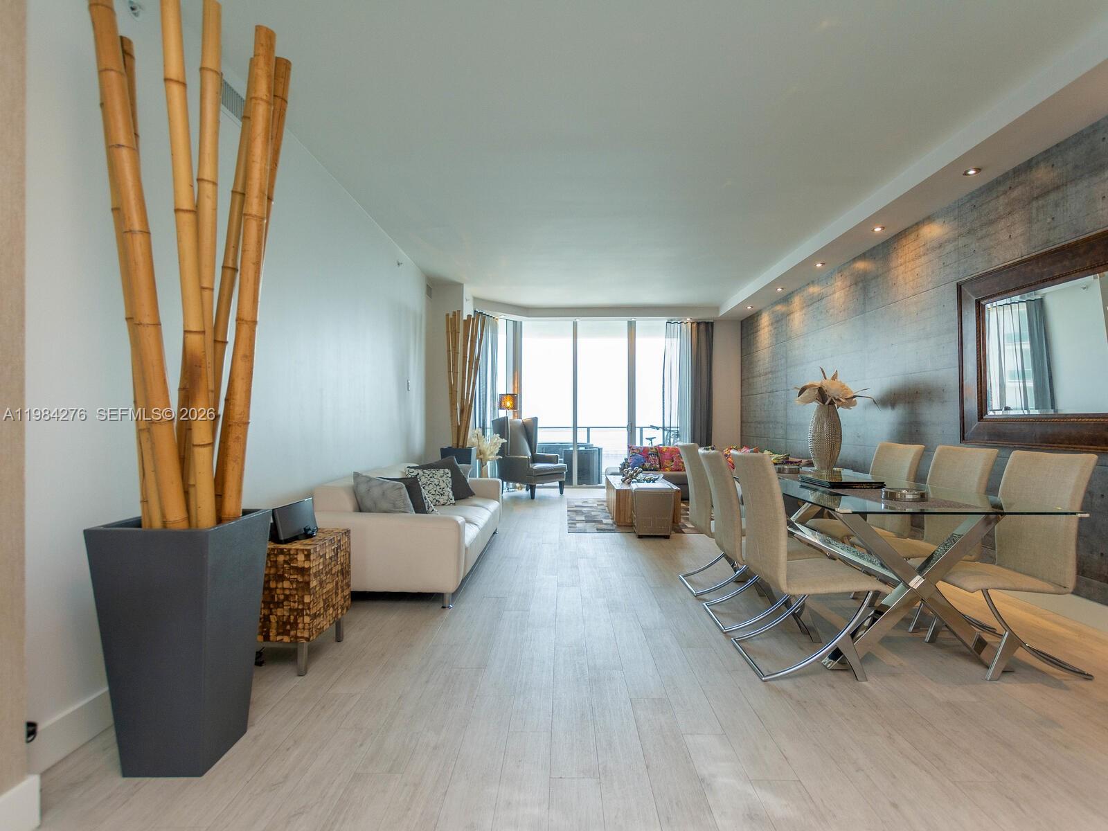 A modern living and dining area features light wood flooring, a concrete wall, and bamboo decor — 1300 Brickell Bay Dr # 3804, Miami FL 33131, MIAMI, FL