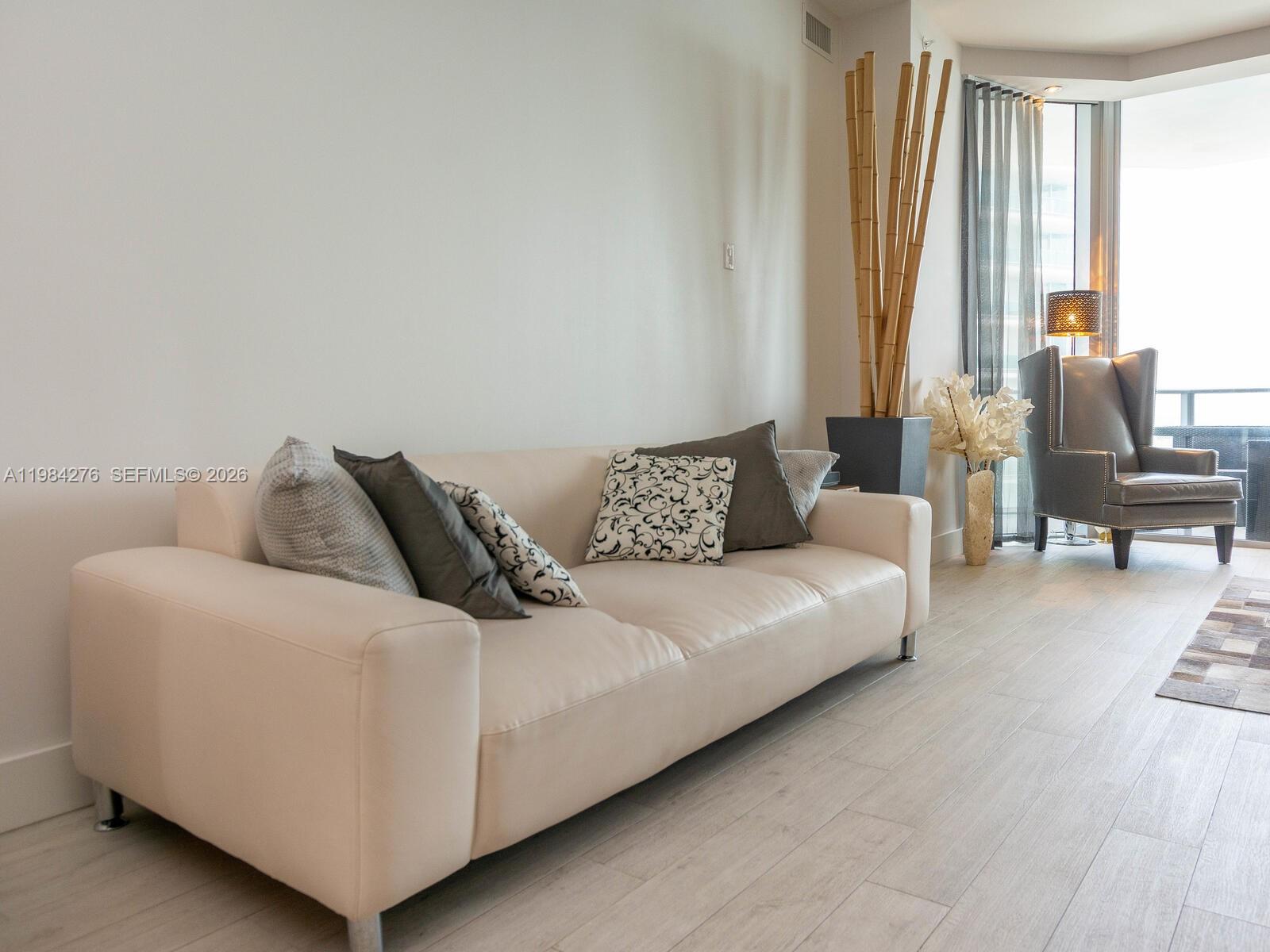 A living room features a cream-colored sofa, light wood flooring, and a tall bamboo arrangement — 1300 Brickell Bay Dr # 3804, Miami FL 33131, MIAMI, FL