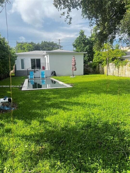 A backyard features a rectangular swimming pool, two blue chairs, and a white house — 15 NW 52nd St, Miami FL 33127, MIAMI, FL
