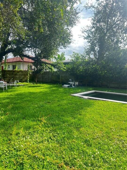 A backyard features a green lawn, a rectangular swimming pool, and mature trees — 15 NW 52nd St, Miami FL 33127, MIAMI, FL