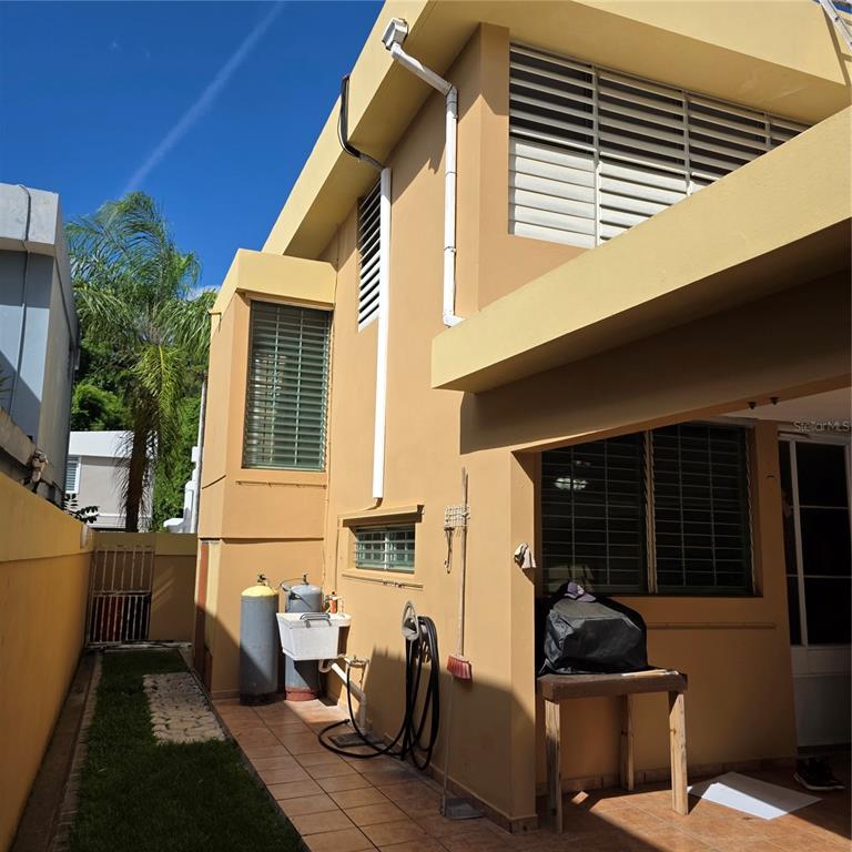 A tan two-story house exterior features a tiled patio, gas tanks, and louvered windows — 512 CALLE BROMELIA, CAROLINA, PR