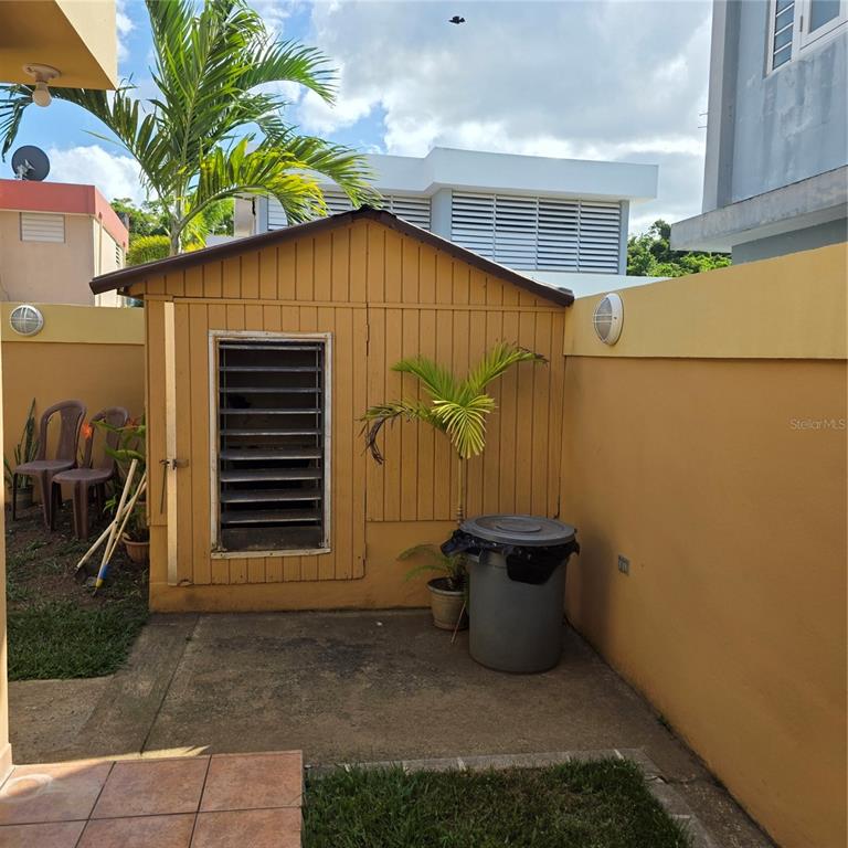 A yellow wooden shed sits on a concrete patio next to a tan wall — 512 CALLE BROMELIA, CAROLINA, PR