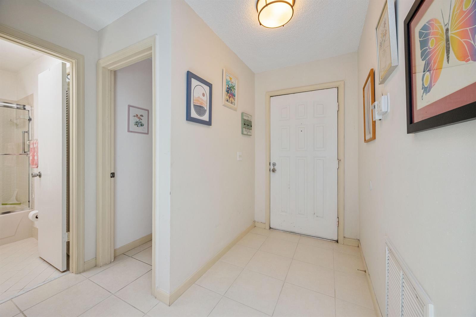 A tiled entryway features a white front door, a bathroom doorway, and wall-mounted artwork — 22 Ridge Pointe Drive # C, Boynton Beach FL 33435, BOYNTON BEACH, FL